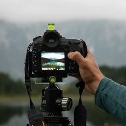 Eine Hand mit einer Kamera, die vor eine Bergkulisse gehalten wird 