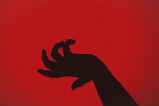 Der Schatten einer verkrampften Hand vor einer roten Wand