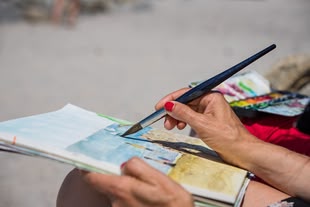 Blick auf die Hände einer Urban Sketcherin, die draußen mit einem Pinsel etwas malt