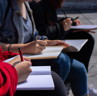 Drei Personen sitzen draußen nebeneinander und zeichnen in ihre Skizzenbücher