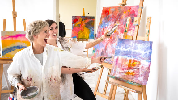 Dozentin Tanja Strickrot und Teilnehmerin stehend lachend vor einem Gemälde