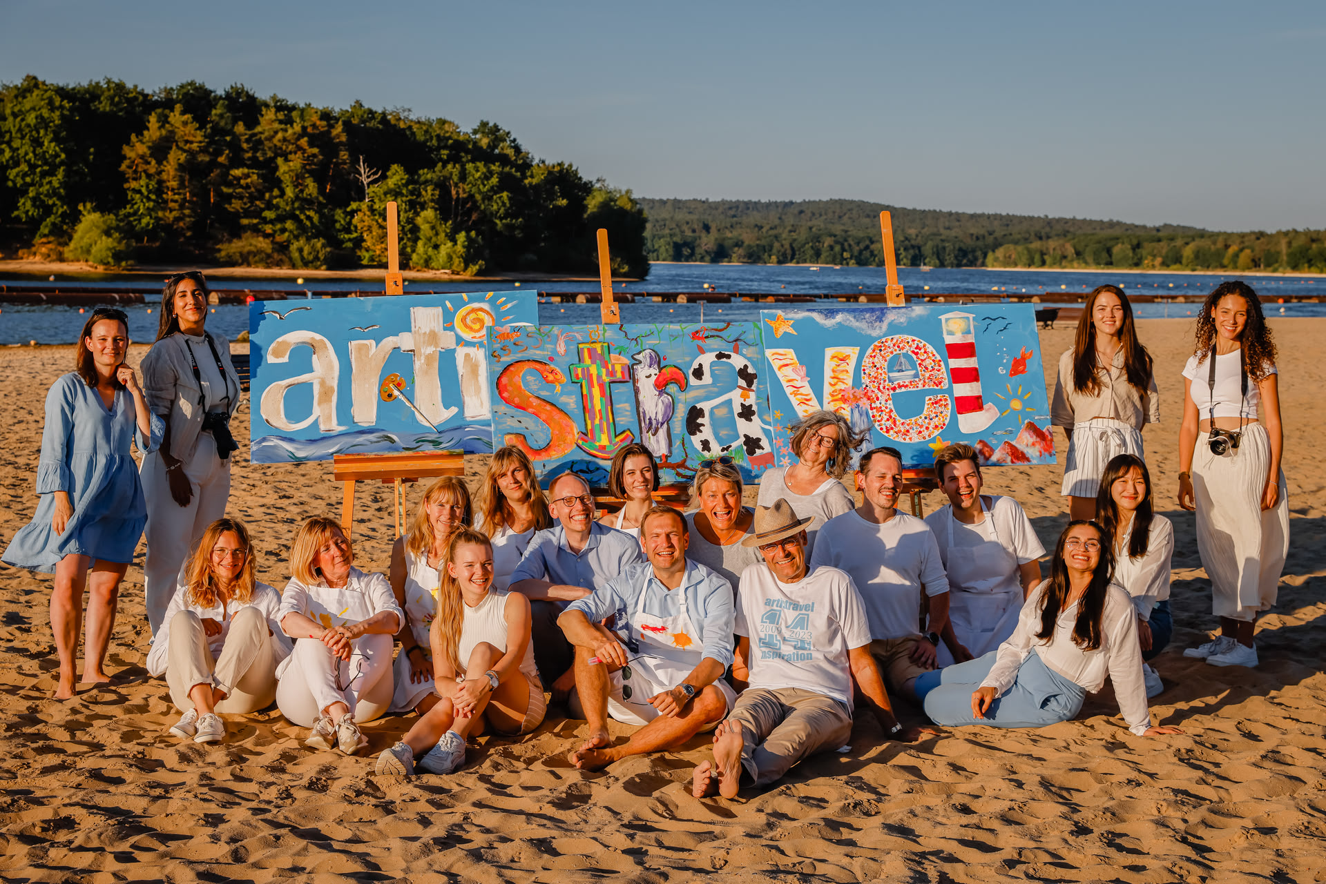 Gruppenbild des artistravel-Teams am Strand vor 3 Leinwänden, auf die das artistravel-Logo gemalt wurde