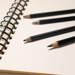 4 Bleistifte liegen auf einem offenen weißen Skizzenbuch