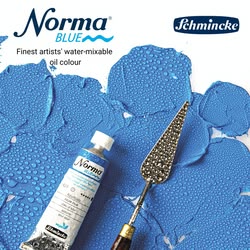 Eine Tube mit blauer Norma Blue Farbe von Schmincke neben einem Spachtel auf blau gemaltem Hintergrund