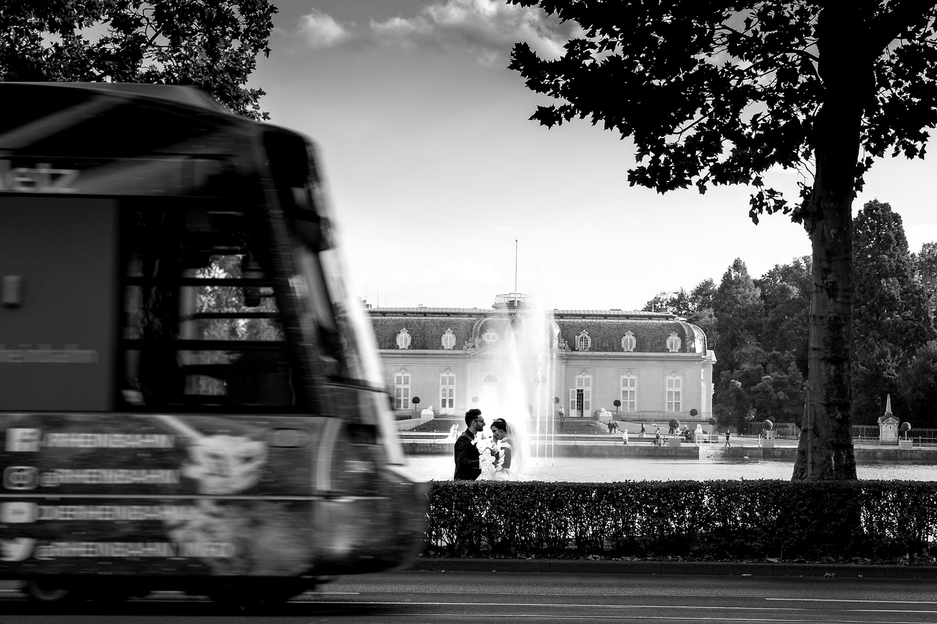 Schwarz-Weiß Bild von einem Brautpaar vor einem Schloss, eine Straßenbahn fährt vorbei