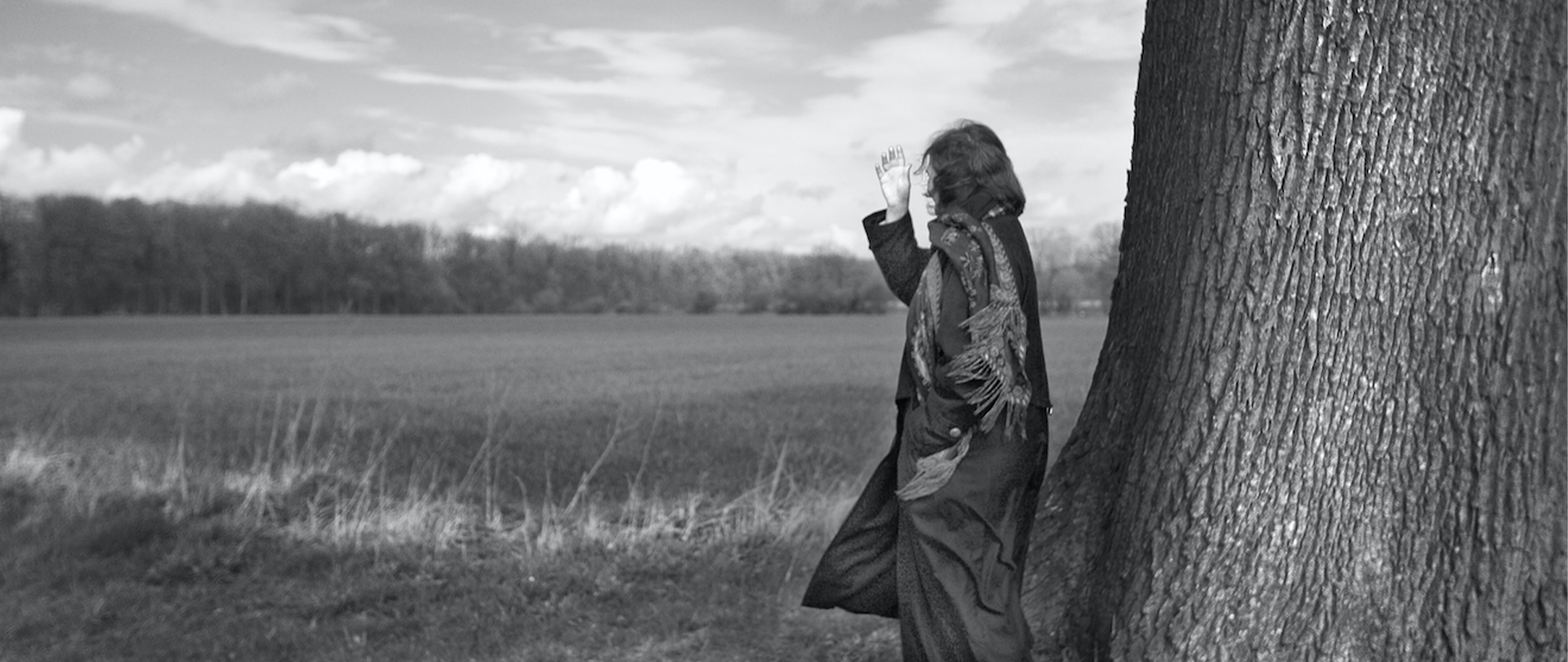 Ein schwarz-weiß Foto, das eine Person neben einem dicken Baumstamm zeigt